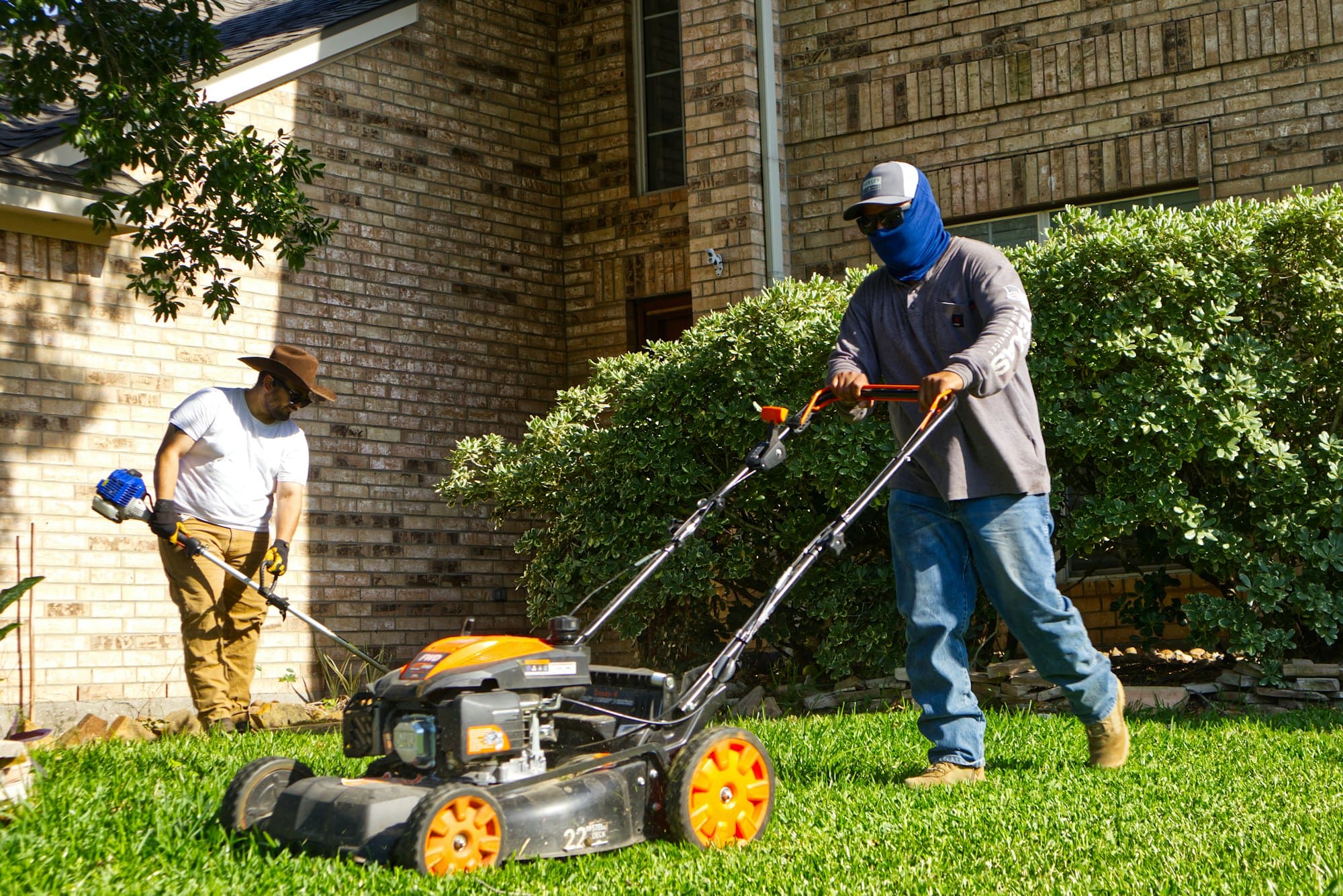 Two crew members mowing and trimming a front lawn