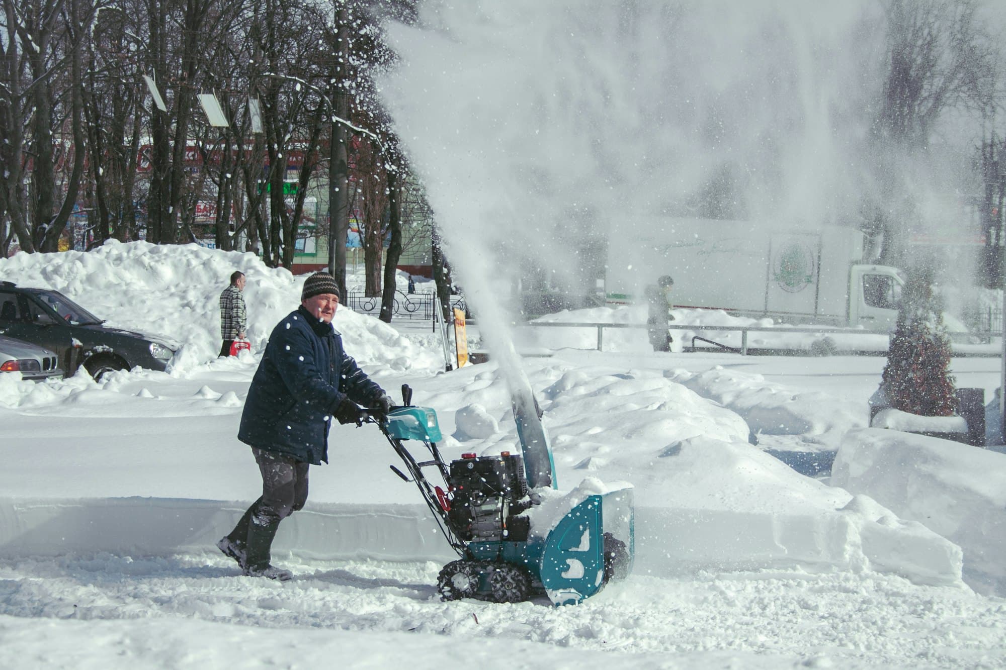 A crew member clearing a sidewalk with a snow blower in falling snow