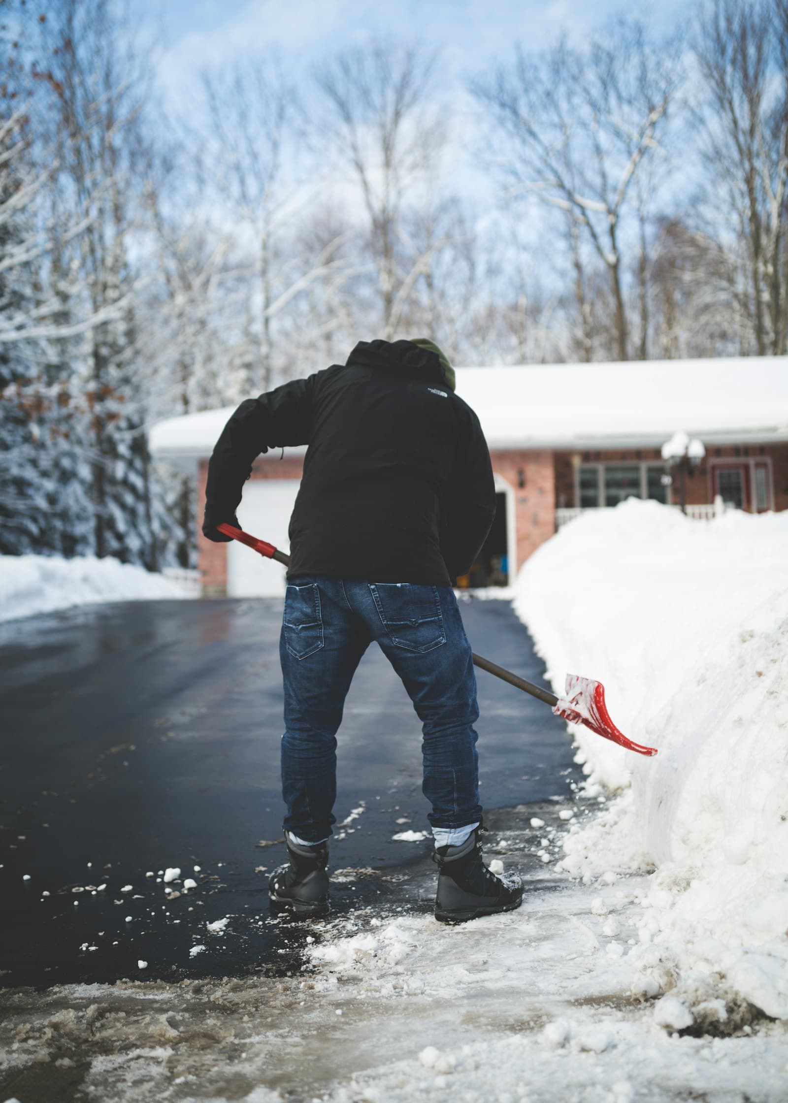 Someone shovelling a snowy driveway in front of a house